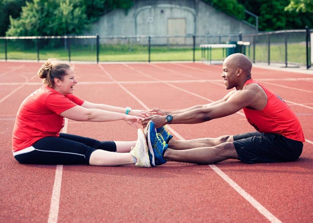 A man and woman stretching together on the track.