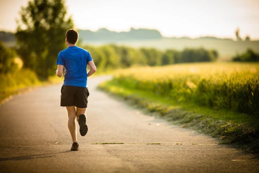 A male athlete running on a dirt road outside.