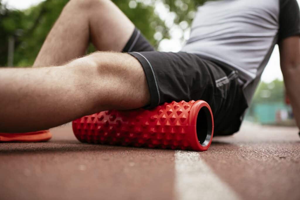 A man foam rolling his hamstrings on a track.