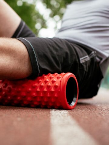 A man with a foam roller under his hamstrings on a track.