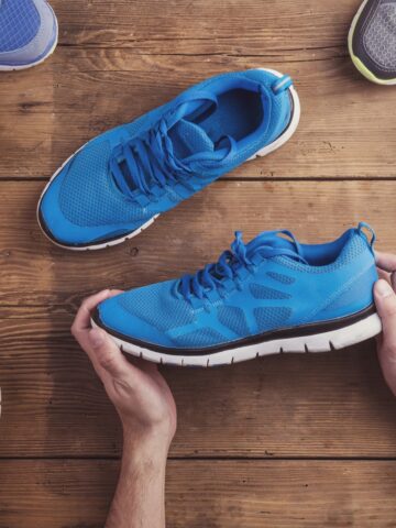 A man holding a pair of memory foam sneakers on a wooden backdrop.