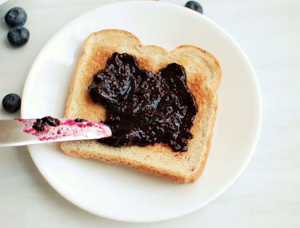 A knife spreading blueberry chia jam on toast.