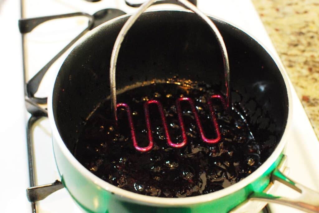 A potato masher mashing blueberries in a pot.