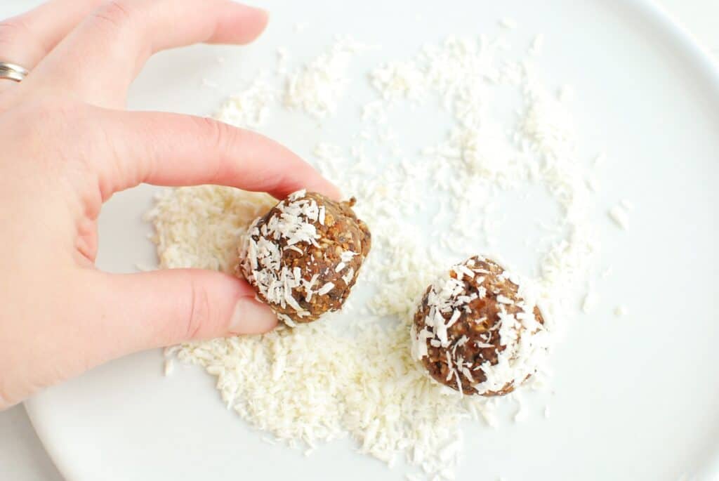 A woman rolling an energy ball in shredded coconut.