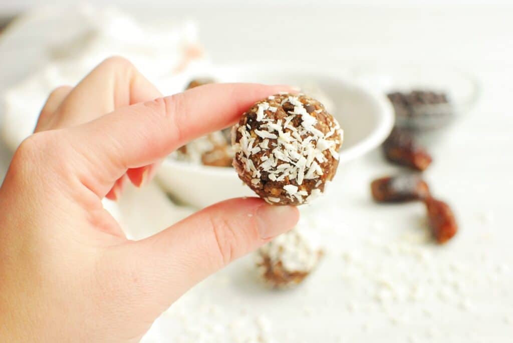 A woman's hand holding a coconut almond date ball.