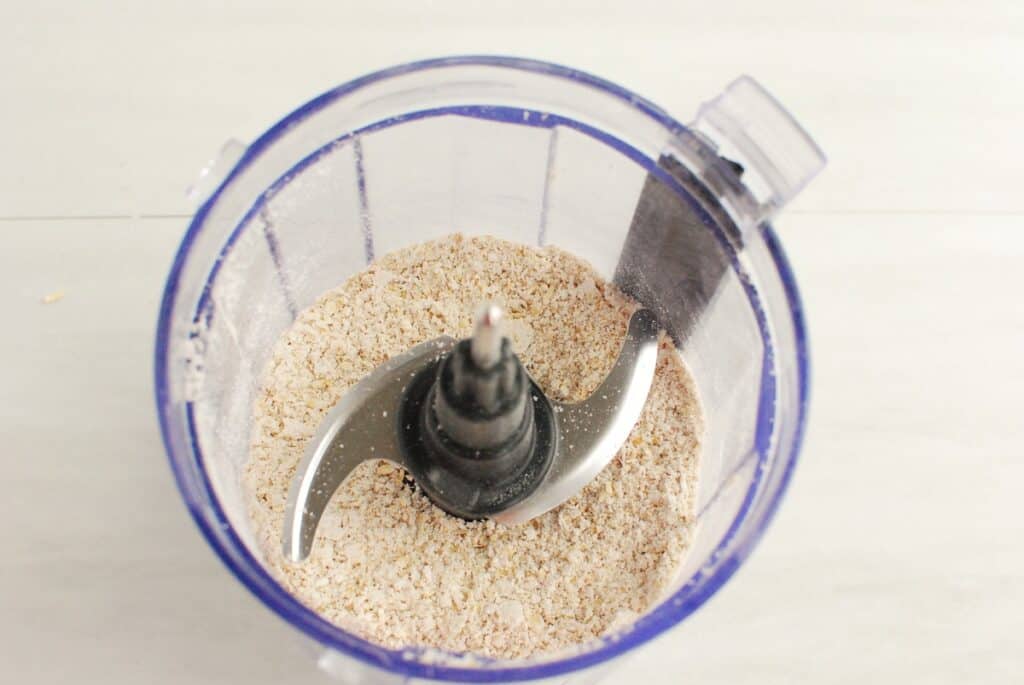 Oats pulsed into a coarse flour in a food processor cup.