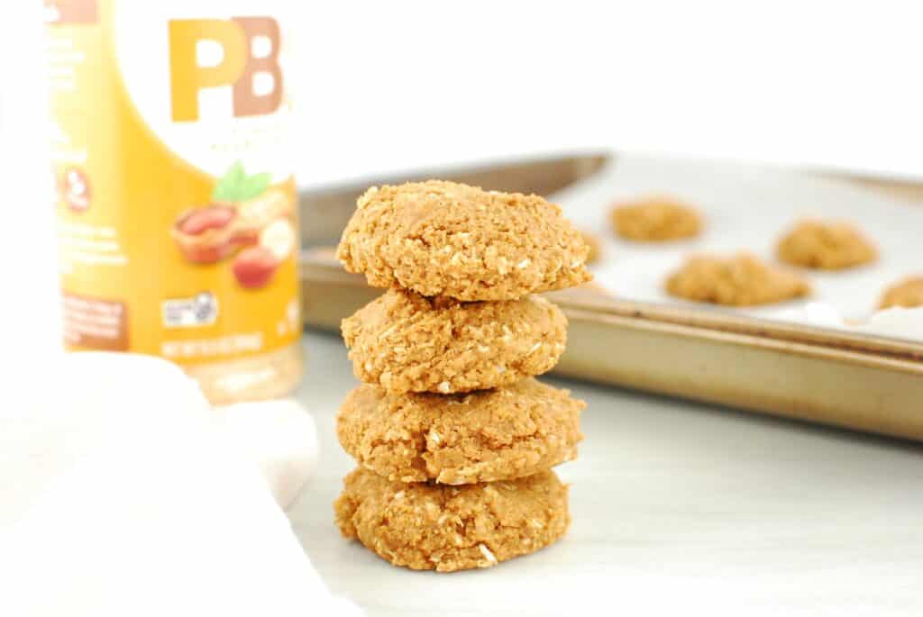 Several powdered peanut butter cookies stacked on top of eachother, with a baking sheet and napkin in the background.