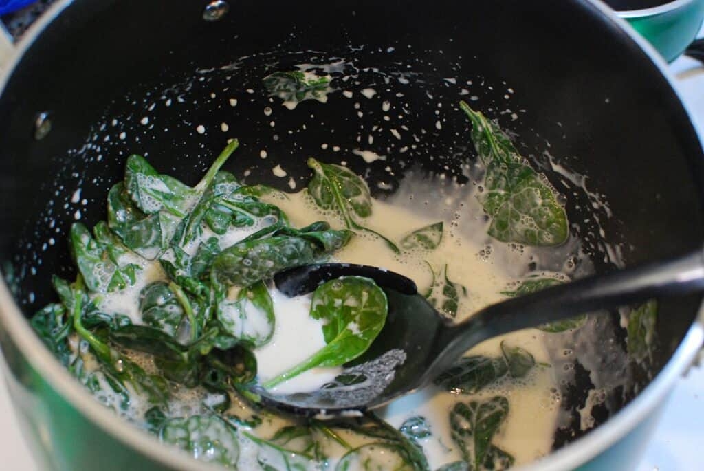 Spinach added to a pot with cream sauce.
