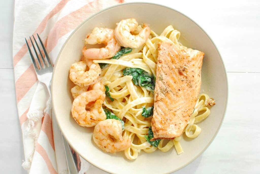 A bowl of shrimp and salmon pasta with a fork and a napkin.