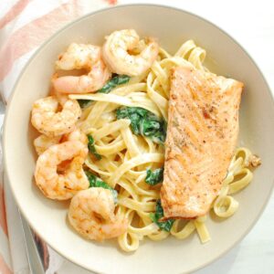 A bowl of shrimp and salmon pasta next to a napkin.