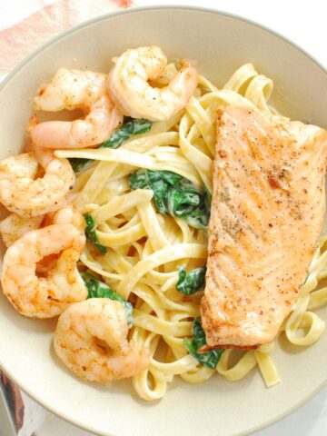 A bowl of shrimp and salmon pasta next to a napkin.