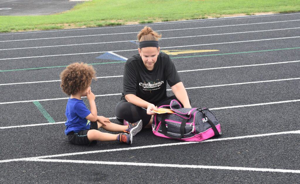 A mom and her son sitting at the track with a duffel bag.