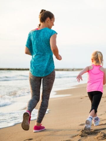 A mom and daughter running together outside on the beach.