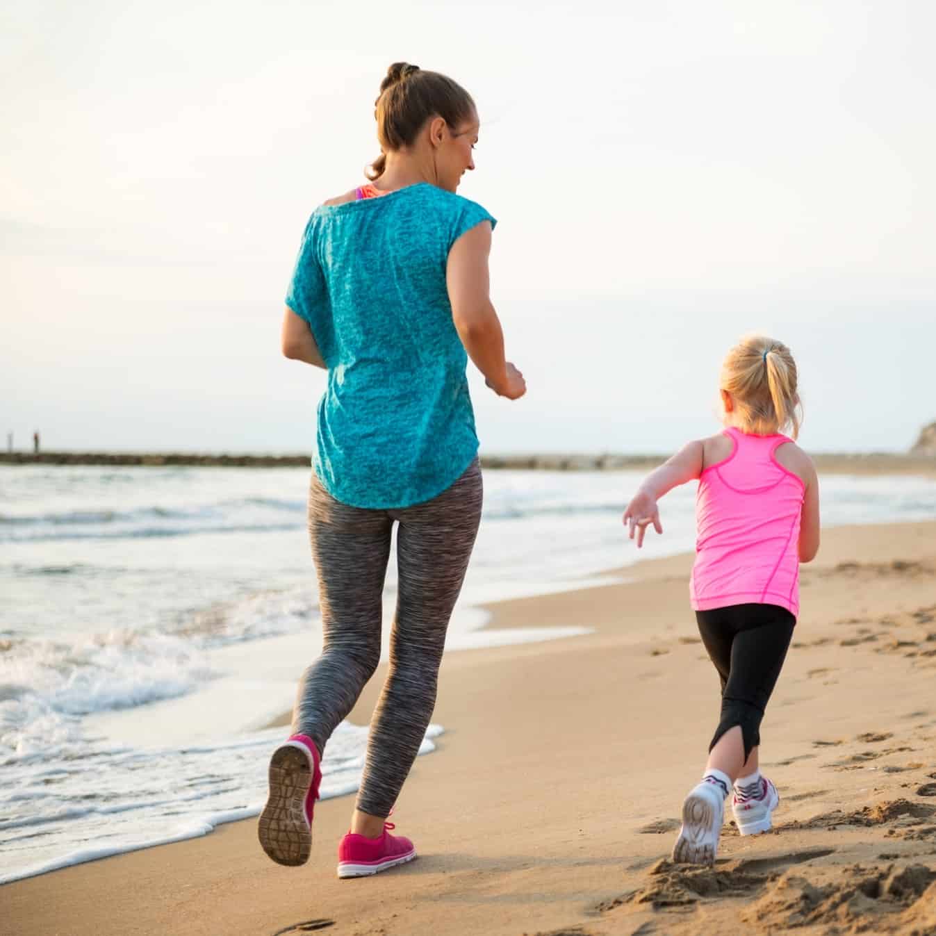 A mom and daughter running together outside on the beach.