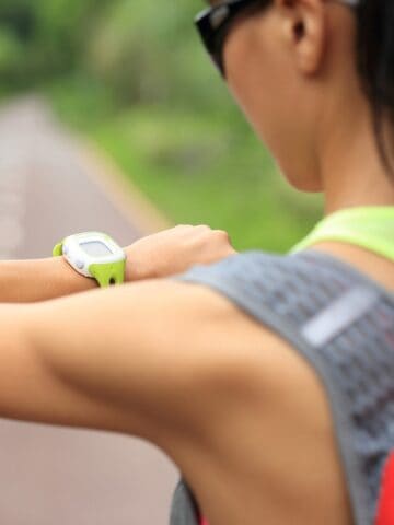 A runner outside in the summer checking her mile time on a watch.