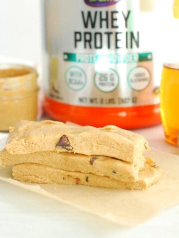 Three peanut butter protein bars next to a container of protein powder, a jar of peanut butter, and a bottle of honey.