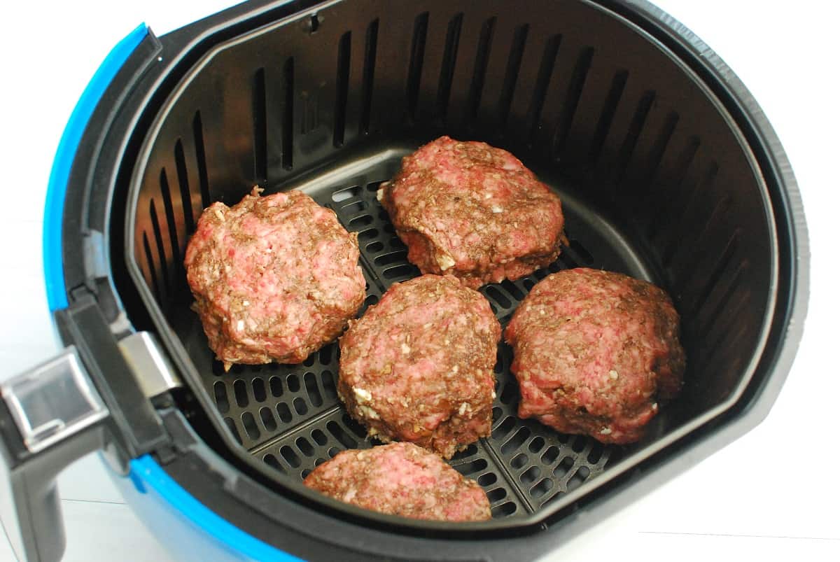 Uncooked lamb burgers in the air fryer basket.