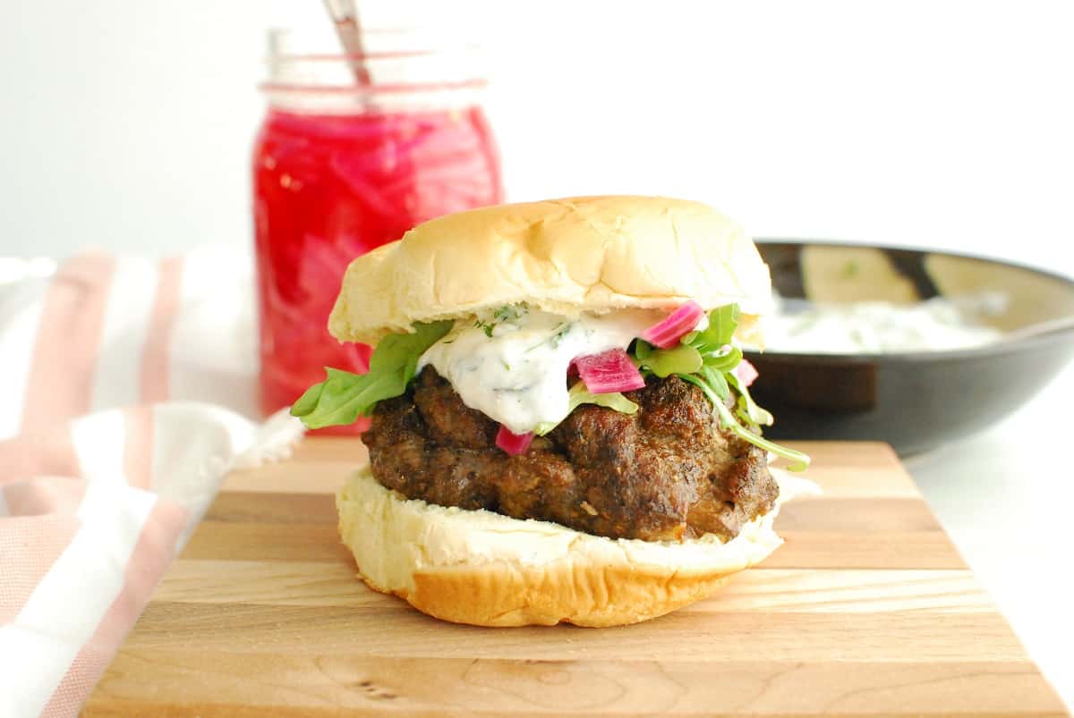 A feta stuffed air fryer lamb burger on a wooden board with pickled onions in the background.