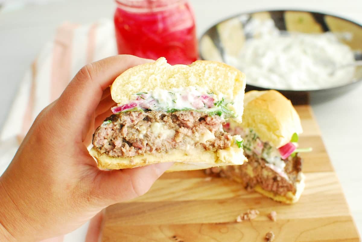 A woman's hand holding half of an air fryer feta stuffed lamb burger.