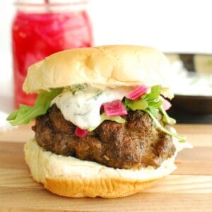 A feta stuffed lamb burger on a bun on a wooden serving board.