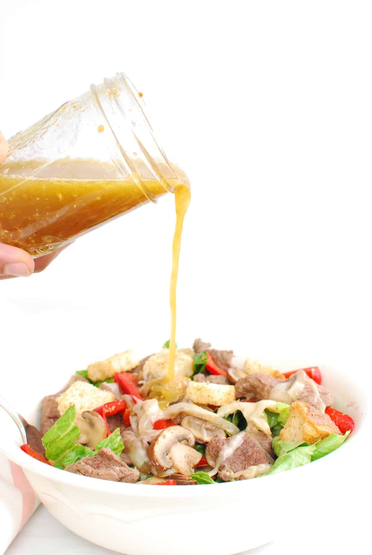 A woman's hand pouring salad dressing over the salad.