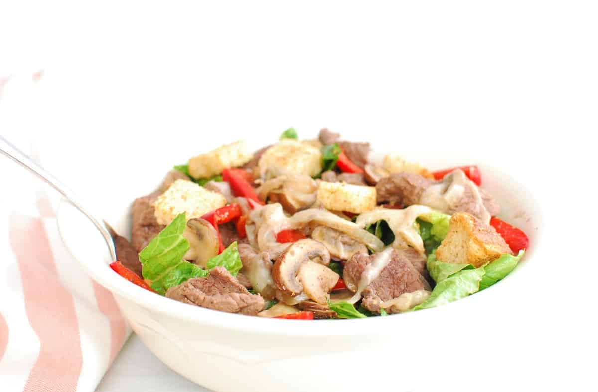 A bowl of cheesesteak salad with a fork stuck in it.