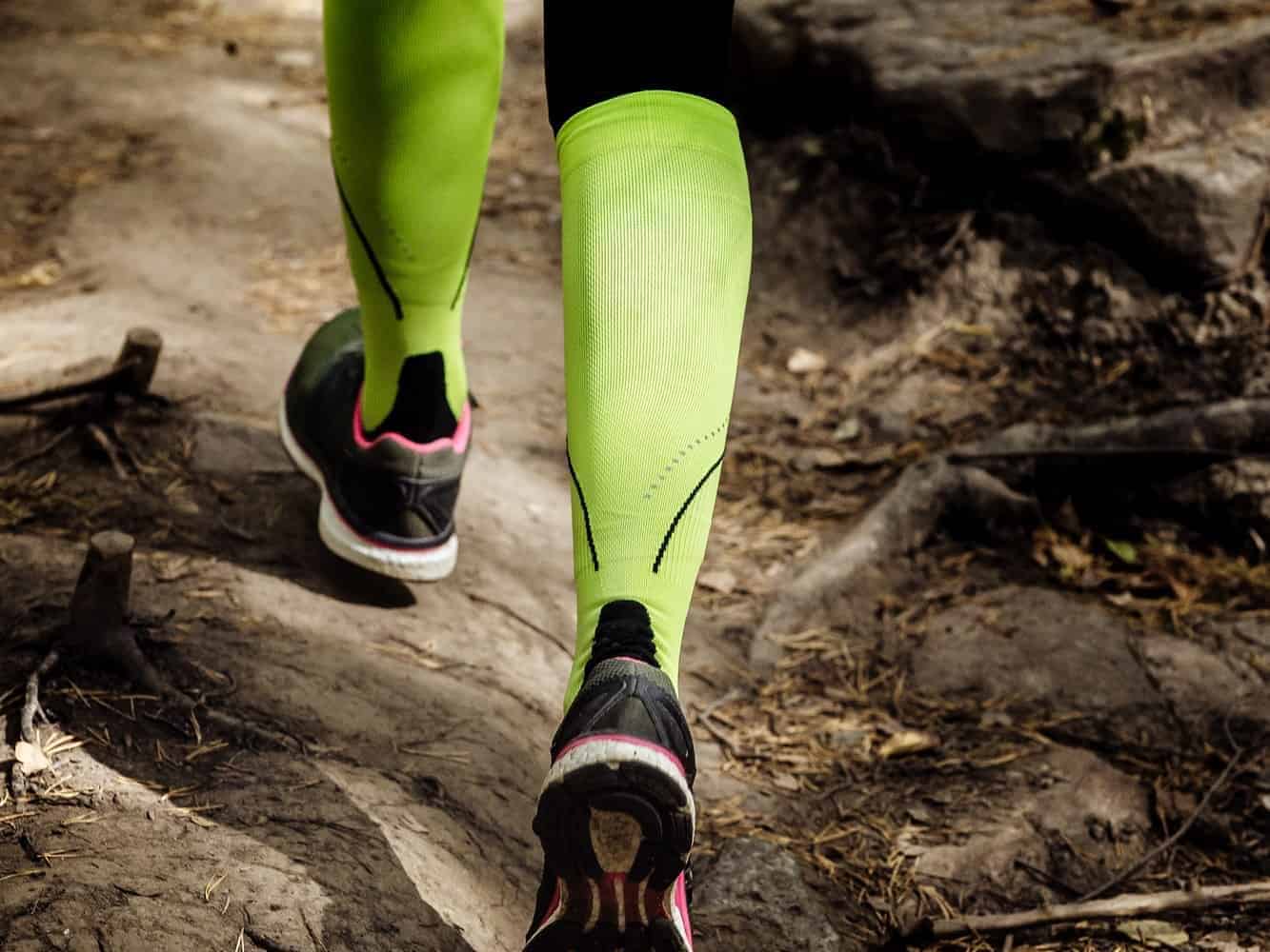 A woman's legs with compression socks on, running on a trail.