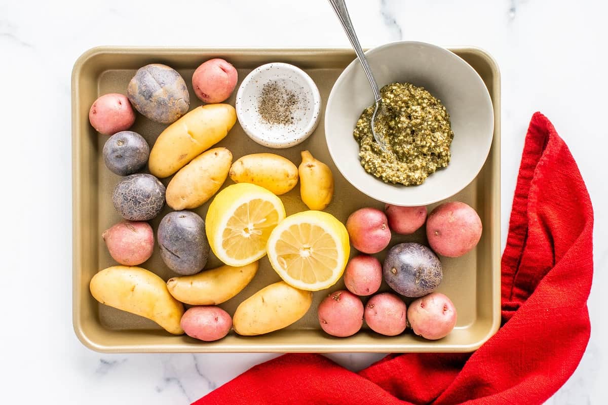 Potatoes, lemon, salt, pepper, and pesto on a tray.