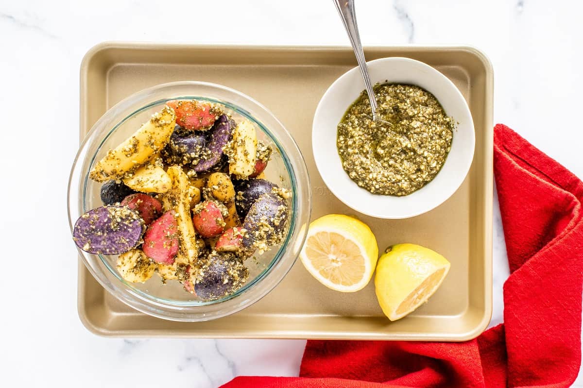 Mixing potatoes in a bowl with pesto, lemon juice, salt, and pepper.