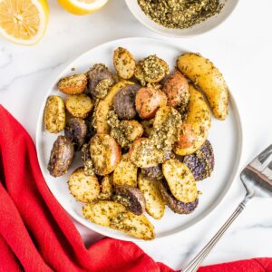 A plate of pesto roasted potatoes next to a red napkin and a fork.