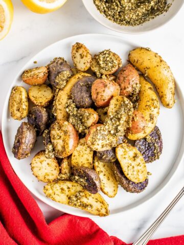 A plate of pesto roasted potatoes next to a red napkin and a fork.