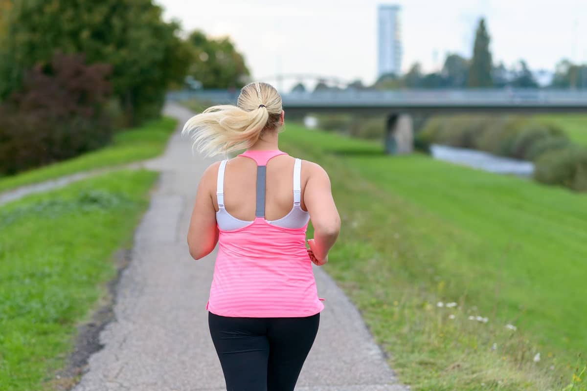 A woman running in a pink tank top on a path outside.