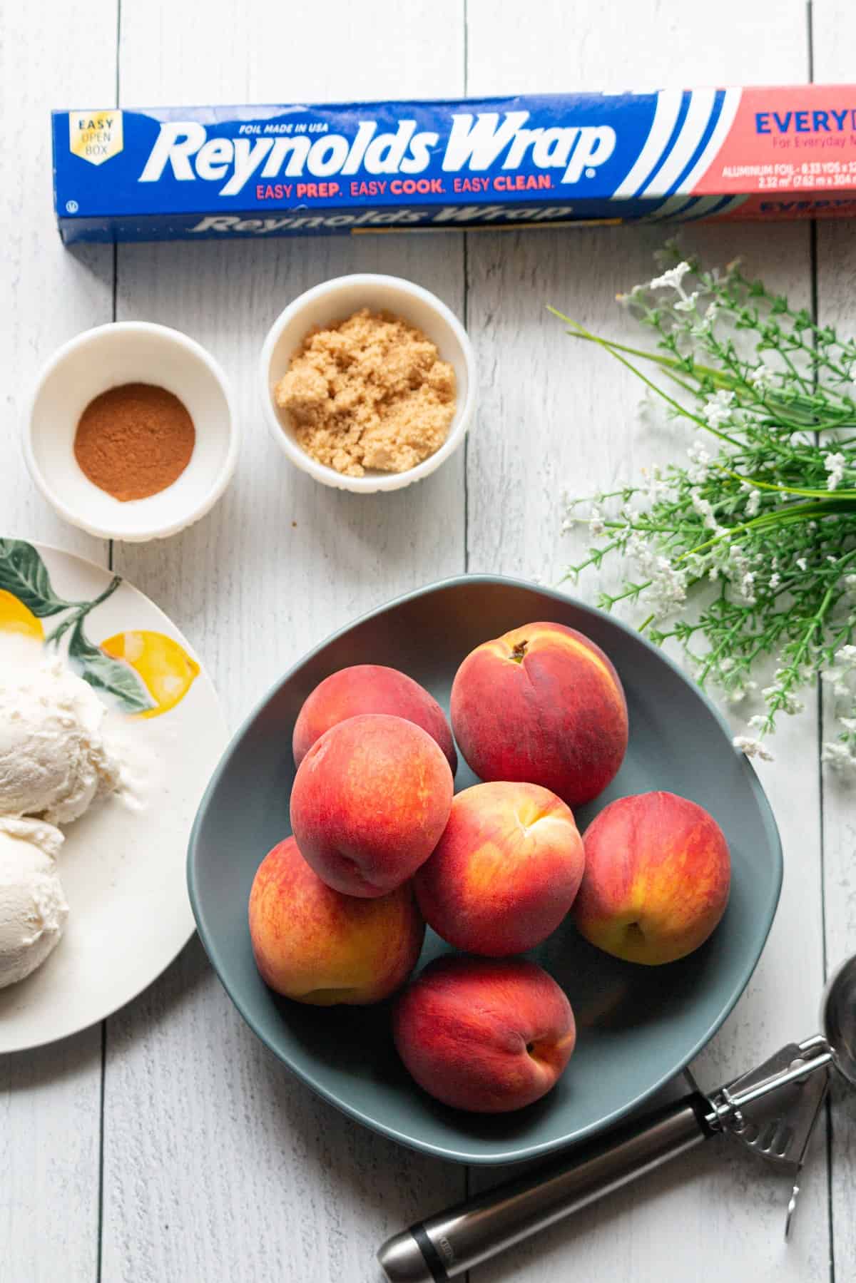 Peaches, brown sugar, cinnamon, and aluminum foil on a table.