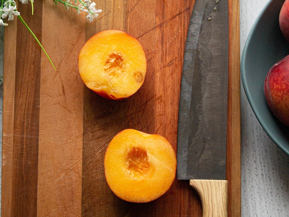 Two peach halves on a cutting board next to a knife.