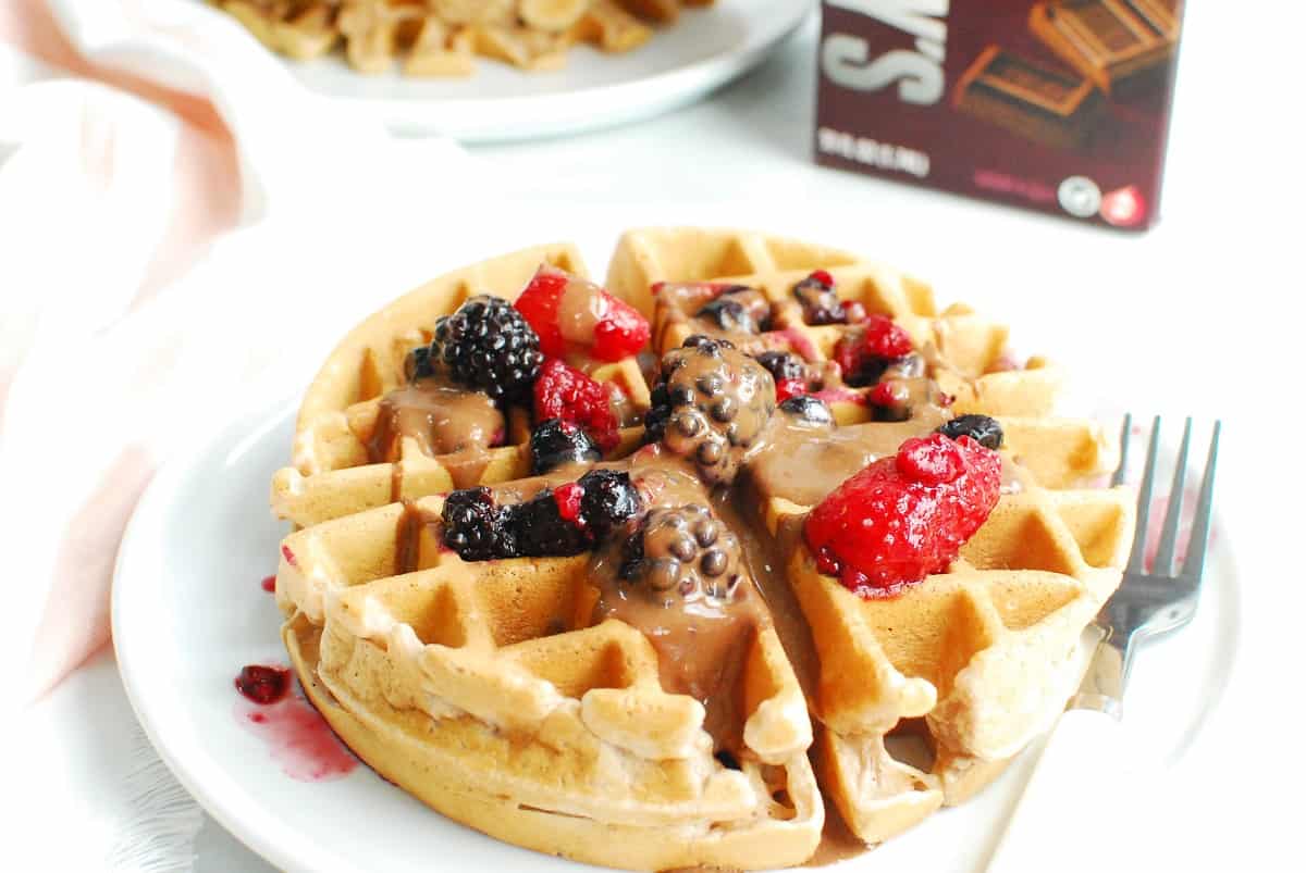 A chocolate milk waffle topped with berries and chocolate peanut butter sauce.