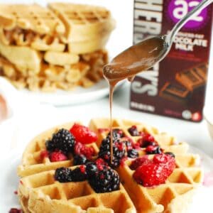 A chocolate milk waffle being drizzled with chocolate peanut butter sauce.