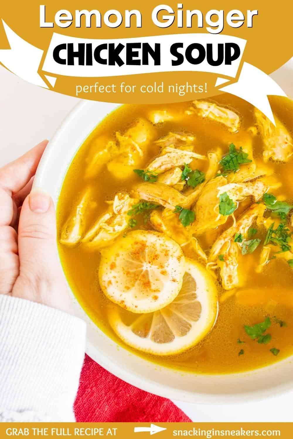 A bowl of lemon ginger chicken soup with a woman's hand holding the bowl.