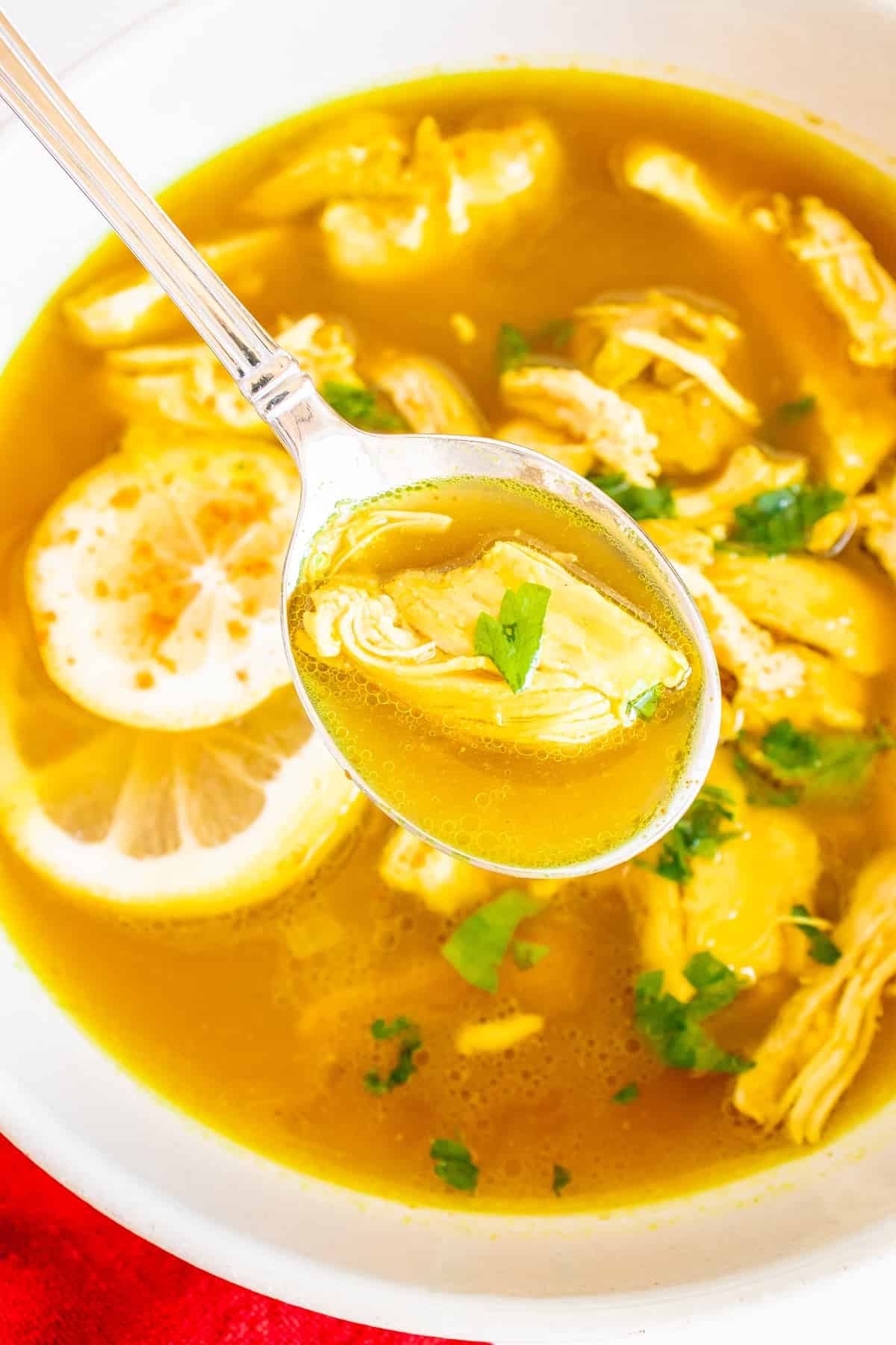 A spoon digging into a bowl of ginger lemon chicken soup.