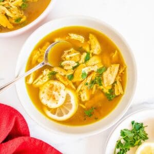 A bowl of lemon ginger chicken soup with a spoon in it and a red napkin next to it.