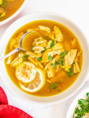 A bowl of lemon ginger chicken soup with a spoon in it and a red napkin next to it.