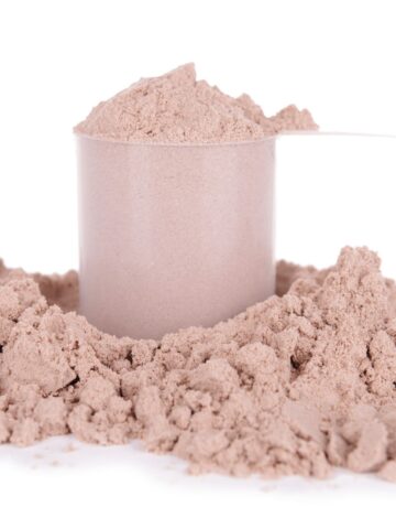 A large scoop of protein powder with more powder scattered around it.