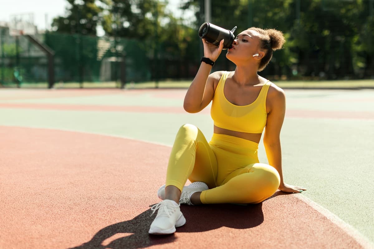 A female athlete drinking a protein shake at a track.