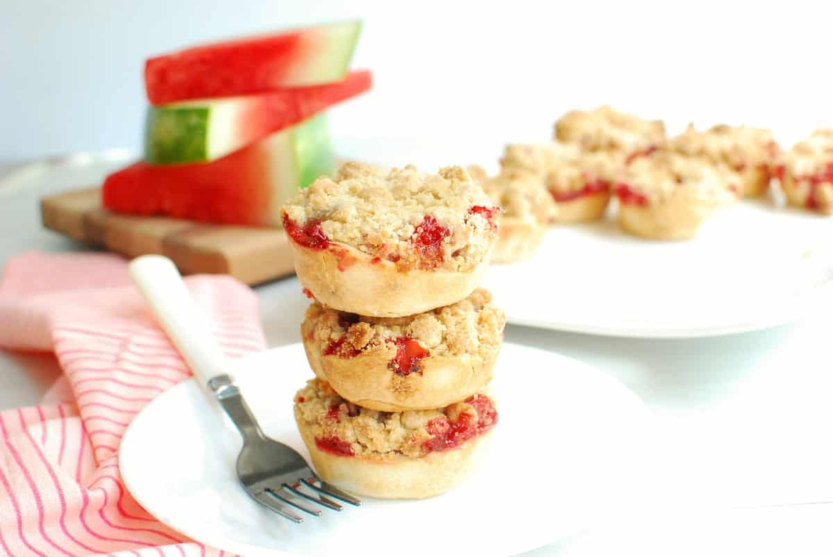 Three mini watermelon rind strawberry pies on a plate next to a fork and napkin.