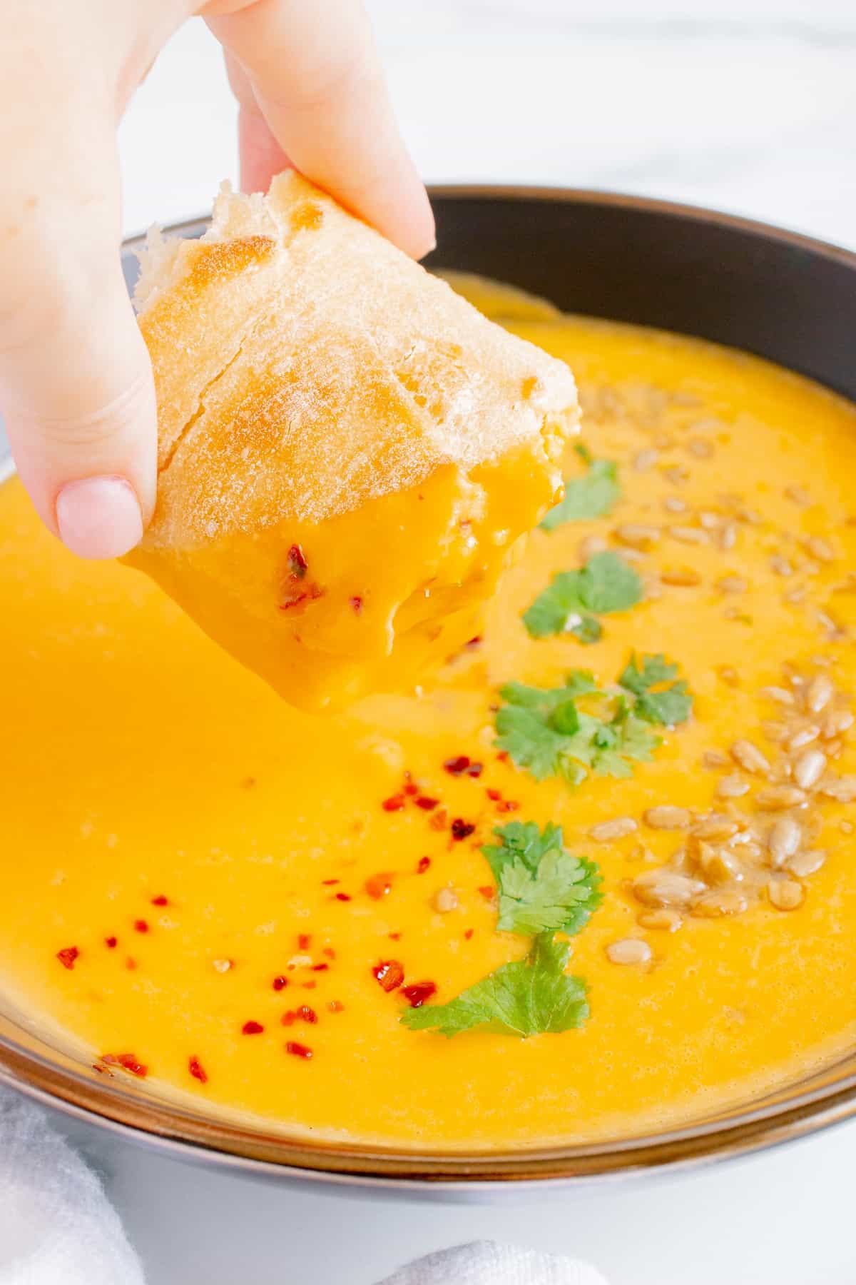 A woman dipping a piece of bread in butternut squash soup.