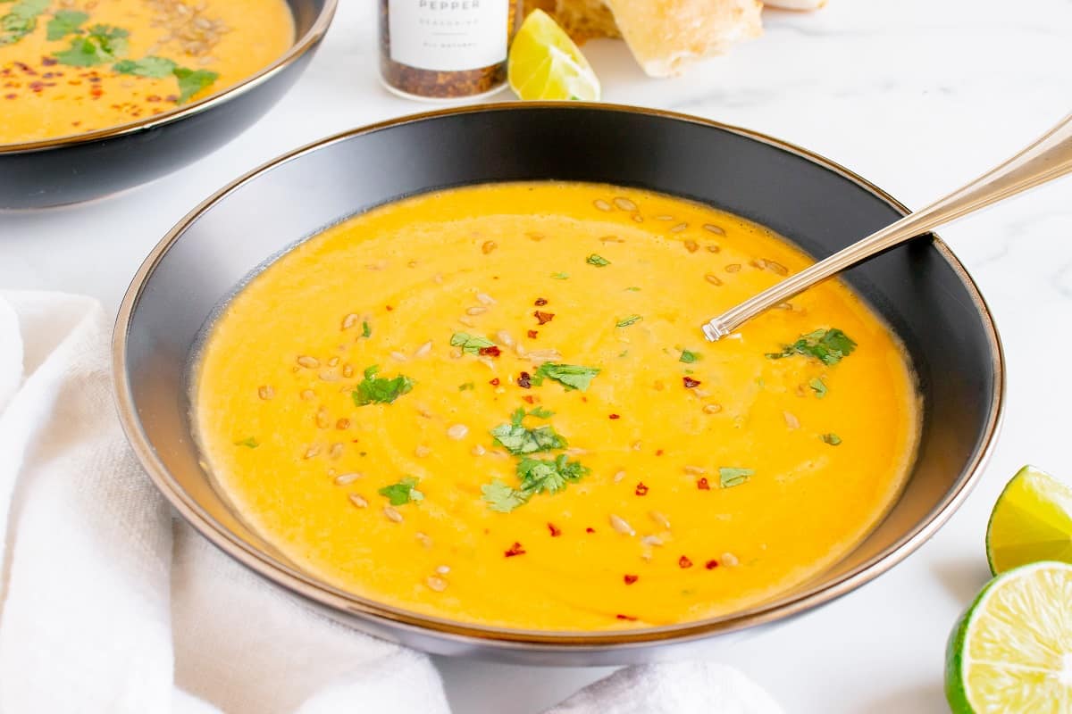 A bowl of butternut squash soup with a spoon in it, next to a napkin and a lime.