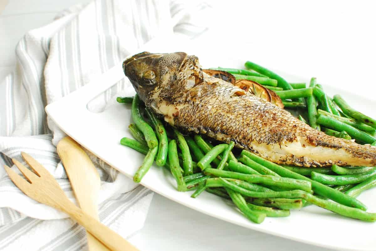 Air fryer whole fish set on top of a plate of green beans.