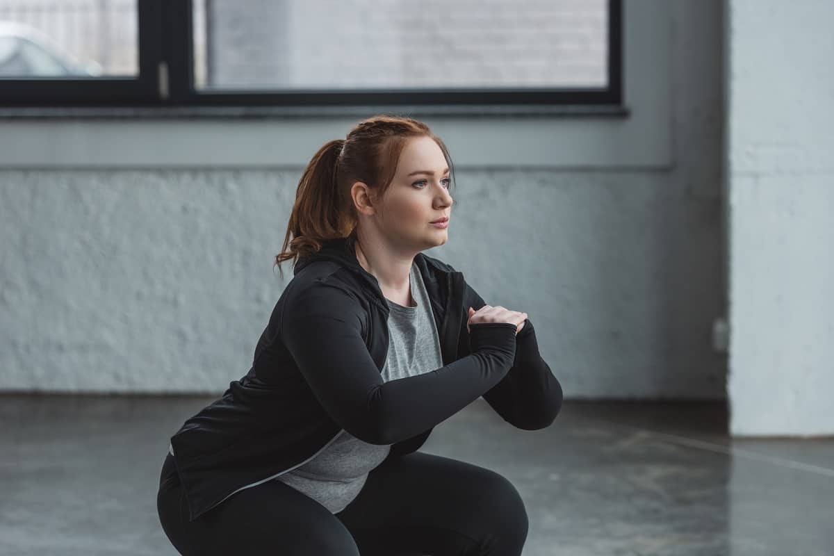 A young woman doing a squat in a gym.