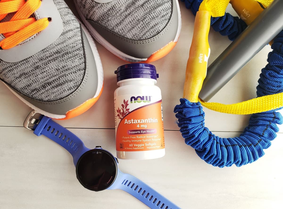 An astaxanthin supplement next to sneakers, a resistance band, and a running watch.