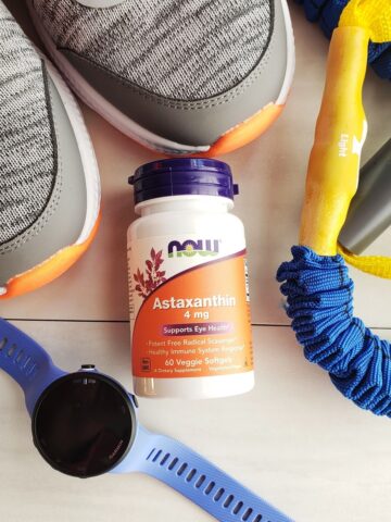 An astaxanthin supplement surrounded by sneakers, a watch, and a resistance band.