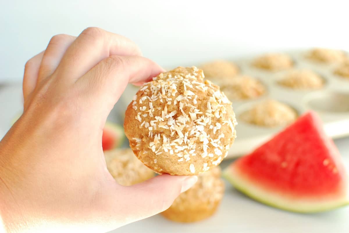 A woman's hand holding a coconut watermelon muffin.